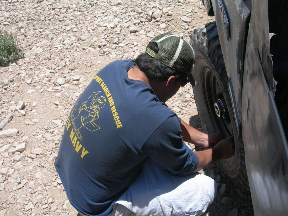 Man in Navy search-and-rescue shirt working at a vehicle wheel on a rocky trail