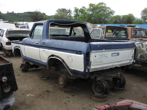 1981 Ford Bronco - Junkyard Bronco body, missing wheels, sits next to other vehicles in a lot.