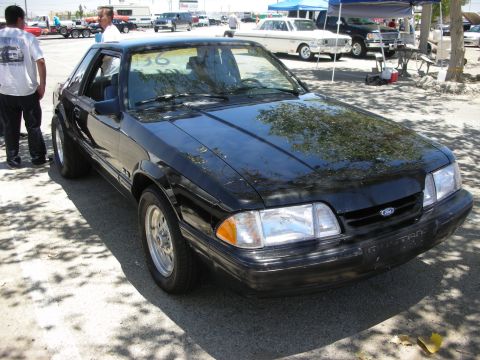 1992 Ford Crown Victoria - A black Ford Mustang is parked outdoors, with other vehicles and tents visible in the background.