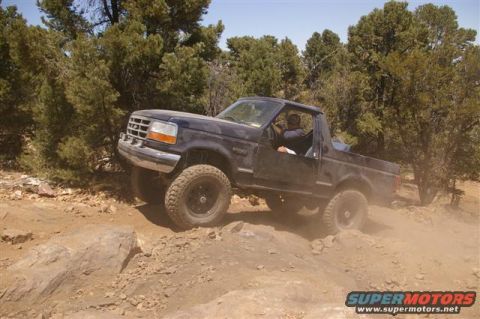 1994 Ford Bronco - A Ford Bronco navigates a rocky off-road trail, kicking up dust.