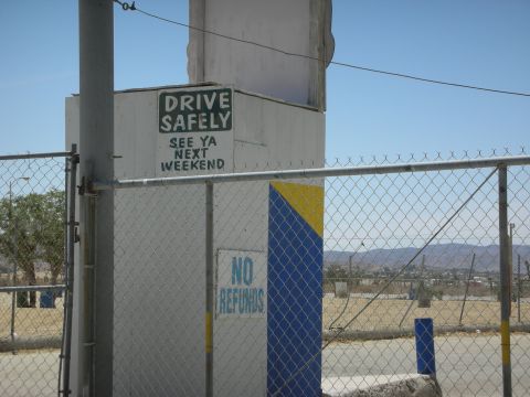 1992 Ford Crown Victoria - A building with signs is visible behind a chain-link fence on a sunny day.