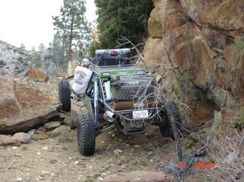 1996 Ford Bronco - An off-road buggy maneuvers through a rocky, mountainous trail with a driver visible from behind.