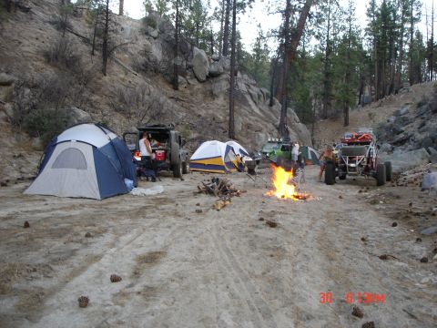 1996 Ford Bronco - Multiple off-road vehicles and tents are set up at a campsite with a roaring campfire.