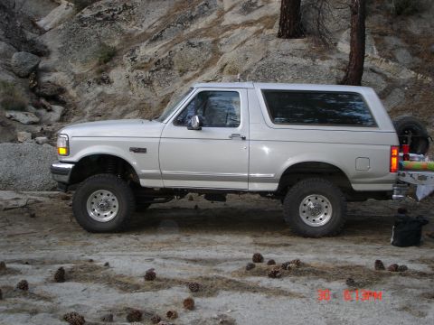 1996 Ford Bronco - A silver 1996 Ford Bronco is parked on a dirt road with rocky hills in the background.
