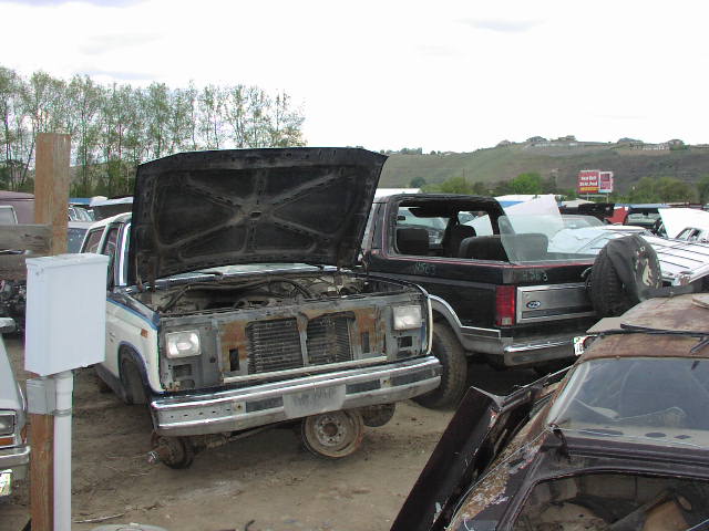 Junkyard scene with a 1980s Ford Bronco and other vehicles, hoods open