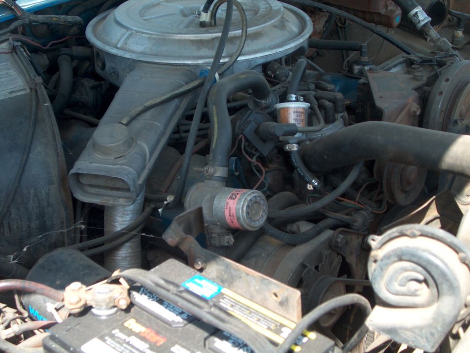 Engine bay with a blue exterior visible, showing a large air cleaner, hoses, and a battery