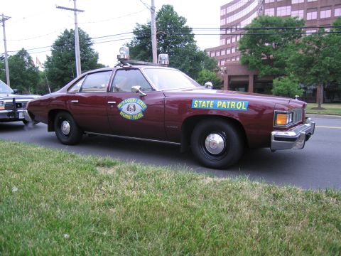 1991 Ford LTD Crown Victoria - maroon Pontiac sedan marked Missouri State Highway Patrol, STATE PATROL on the door, parked at a curb by a grassy verge.
