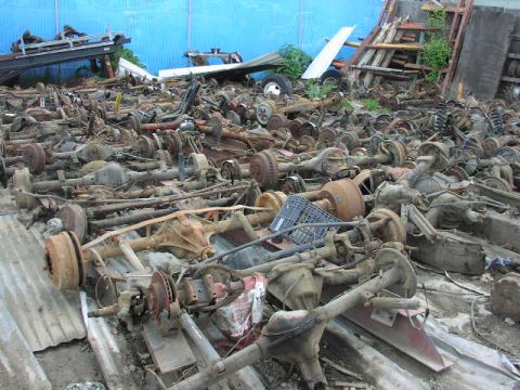 1981 Ford Bronco - A large collection of used vehicle rear axles are piled up in a junkyard.
