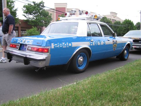 1991 Ford LTD Crown Victoria - Rear quarter view of a blue-and-white NYPD police sedan marked POLICE 2840 HWY 3 with roof lights, parked at a curb.