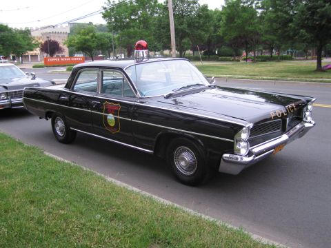 1991 Ford LTD Crown Victoria - black vintage police sedan with a single red roof bubble light and gold door shield parked along a grassy roadside.