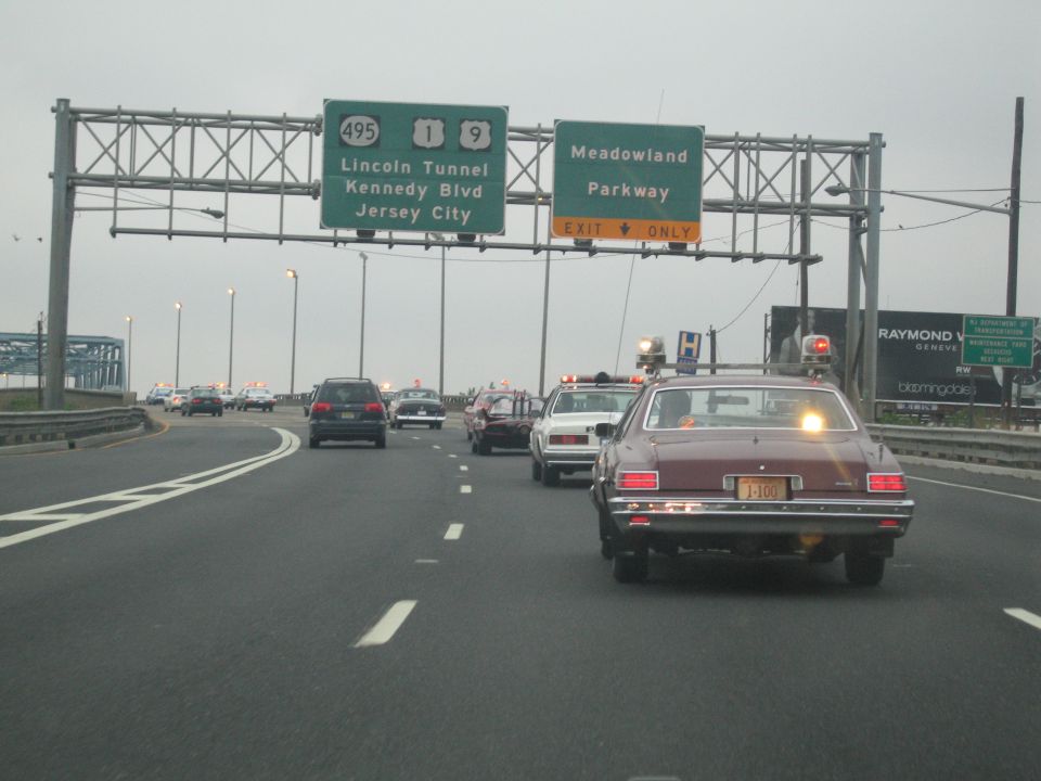 Maroon sedan with roof light on highway near Lincoln Tunnel exit signs