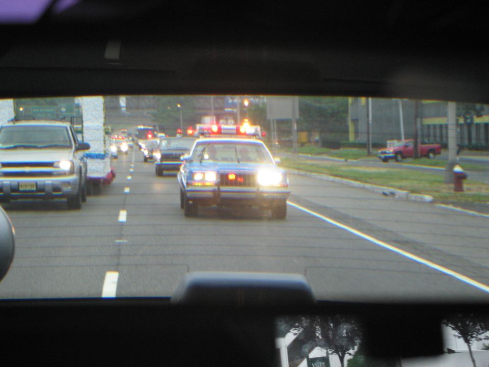 Police car with red emergency lights leading a procession seen through a windshield