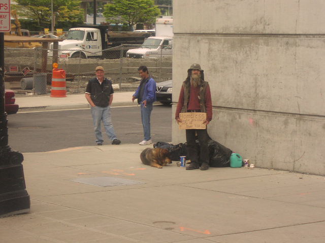 City sidewalk scene with people, a dog, and a white box truck parked behind construction fencing