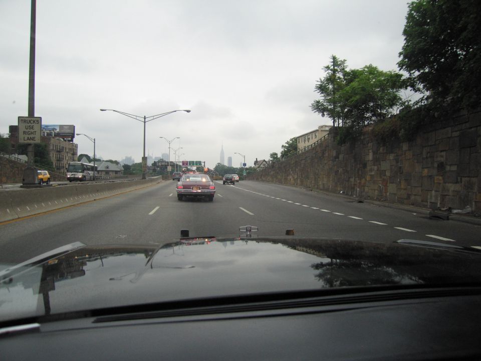 View through windshield of a maroon car ahead on a highway with a distant city skyline
