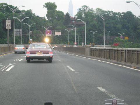 1991 Ford LTD Crown Victoria - maroon station wagon with a single roof beacon travels a roadway flanked by tall streetlights and trees.