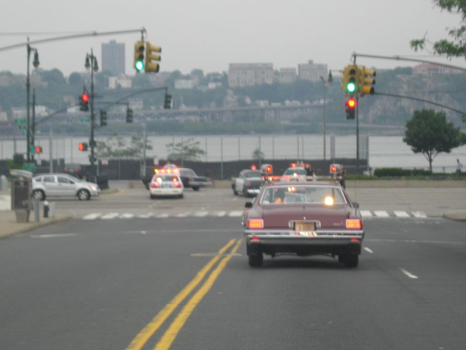 Maroon sedan with roof lights at an intersection with traffic signals and water behind