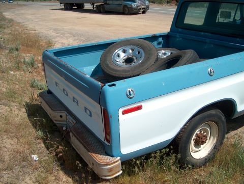 1978 Ford Bronco - Rear view of a 1978 Ford pickup truck bed loaded with spare tires, with a semi-truck visible on the highway.