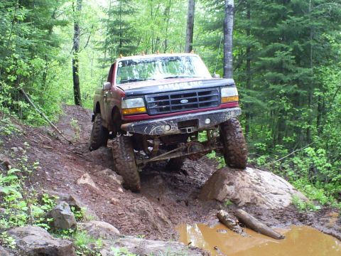 1994 Ford F-250 - This modified Ford F-250 navigates a challenging off-road course with steep inclines and muddy terrain.