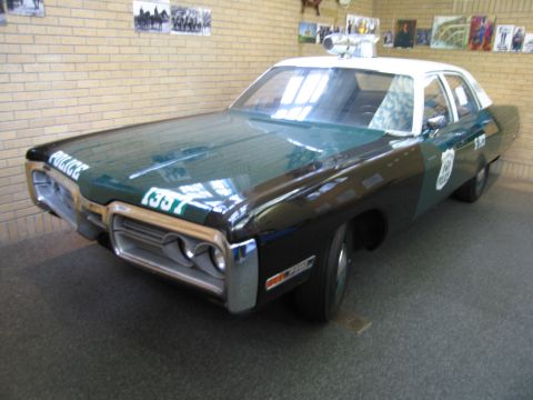 1991 Ford LTD Crown Victoria - restored green and white police sedan lettered POLICE, with roof light bar, stands on indoor exhibit flooring.