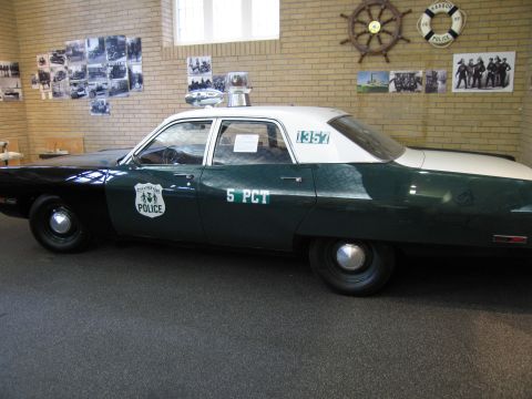 1991 Ford LTD Crown Victoria - Side view of a vintage green and white police car lettered 5 PCT POLICE on indoor museum display before historical photos.