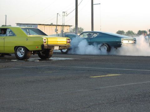 1981 Ford Bronco - Two cars are on a drag strip, with one creating a large cloud of smoke.