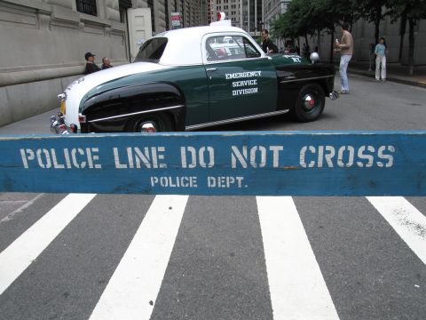 1991 Ford LTD Crown Victoria - vintage green and white police coupe marked Emergency Service Division sits behind a blue POLICE LINE DO NOT CROSS barricade.