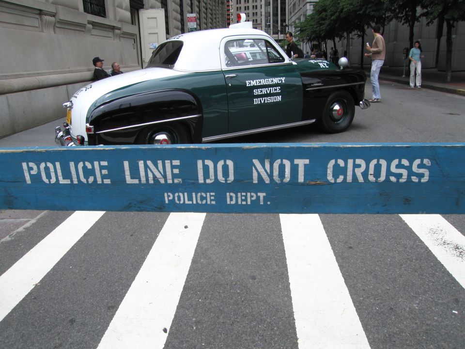 Vintage green and white police coupe behind a POLICE LINE DO NOT CROSS barrier