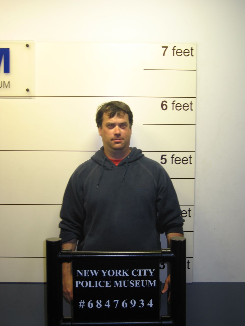 Man in gray hoodie standing against police height chart with New York City Police Museum sign