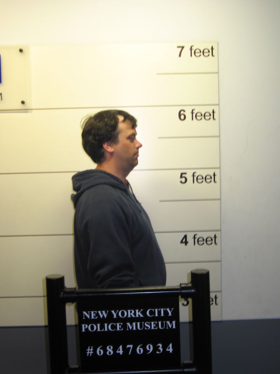 Profile mugshot of man in gray hoodie against police height chart