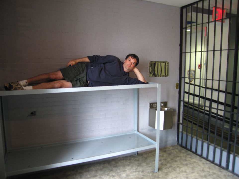 Man reclining on steel bunk shelf inside a mock jail cell