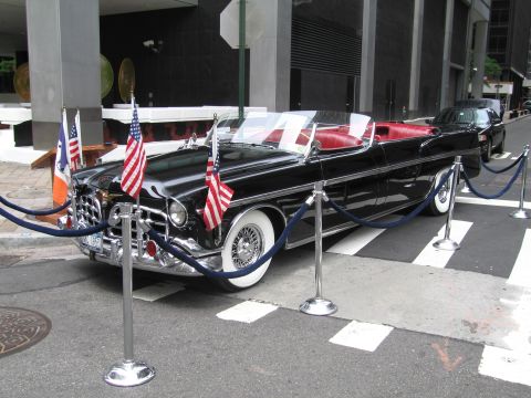 1991 Ford LTD Crown Victoria - long black vintage convertible parade limousine with whitewall wire wheels and American flags, displayed behind blue stanchion ropes by a s…