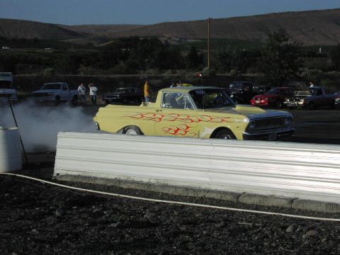 1981 Ford Bronco - Yellow pickup truck with flame decals performing a burnout at a drag race event.