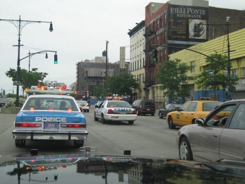 1991 Ford LTD Crown Victoria - Two blue-and-white POLICE cars and a yellow taxi on a city street beneath a Filli Ponte Ristorante building sign with green traffic lights.