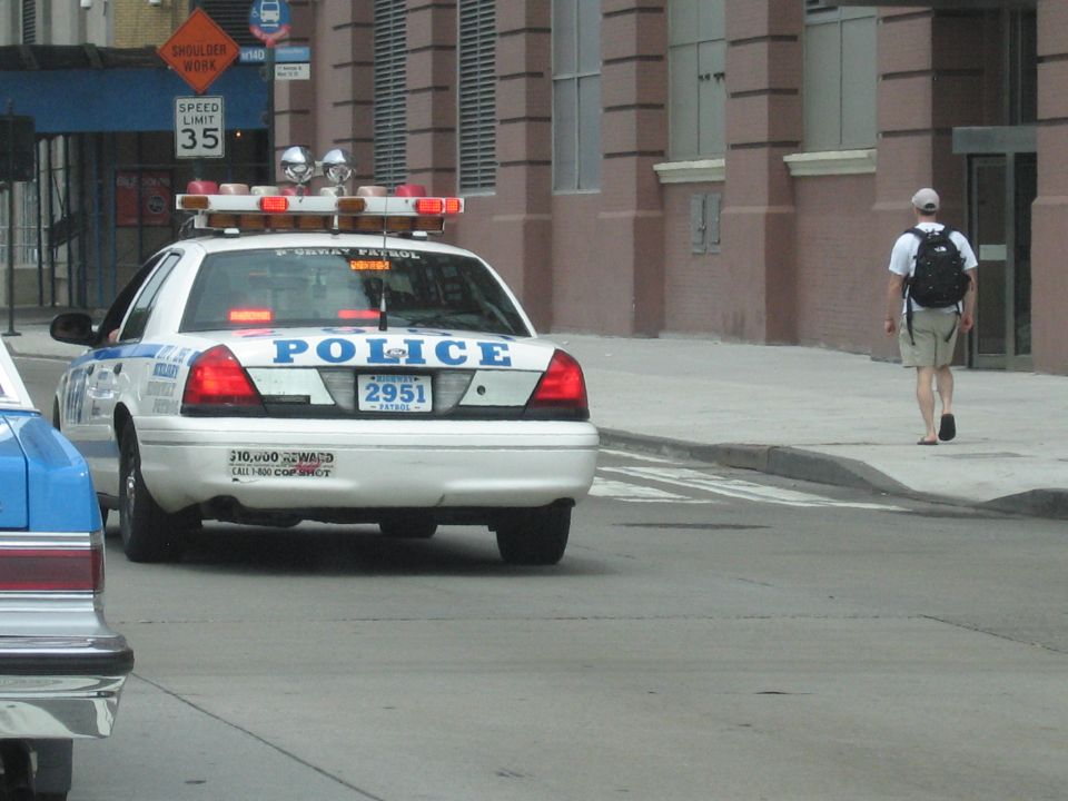 White POLICE car parked at curb as a pedestrian with backpack walks by