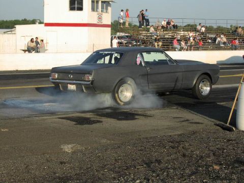 1981 Ford Bronco - A classic Mustang performs a burnout on the drag strip, generating smoke from its tires as spectators watch from the stands.