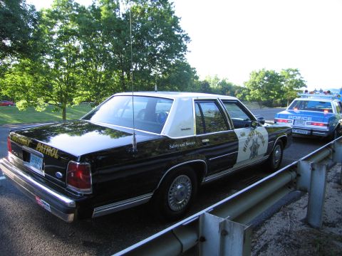 1991 Ford LTD Crown Victoria - black-and-white highway patrol sedan, a Ford LTD Crown Victoria marked Safety and Service, parked by a guardrail beside another vintage pat…