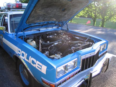 1991 Ford LTD Crown Victoria - blue-and-white sedan marked POLICE stands with its hood raised, exposing the engine bay, beside a green lawn.
