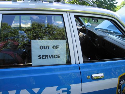 1991 Ford LTD Crown Victoria - blue police car's rear side window holds a white OUT OF SERVICE placard, with the steering wheel and dash visible inside.