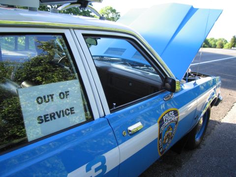 1991 Ford LTD Crown Victoria - blue-and-white police car with raised hood shows a Police Department shield decal and an OUT OF SERVICE sign in the window.