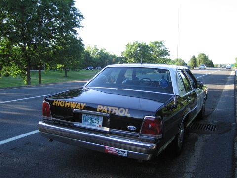 1991 Ford LTD Crown Victoria - black sedan lettered HIGHWAY PATROL with a CHP8849 plate and a Drink & Drive bumper sticker is parked along a tree-lined road.