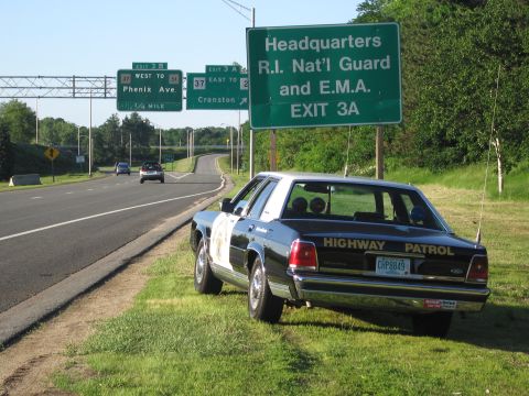 1991 Ford LTD Crown Victoria - black-and-white HIGHWAY PATROL Ford sedan is parked on grass along a highway under green Exit 3A guide signs.