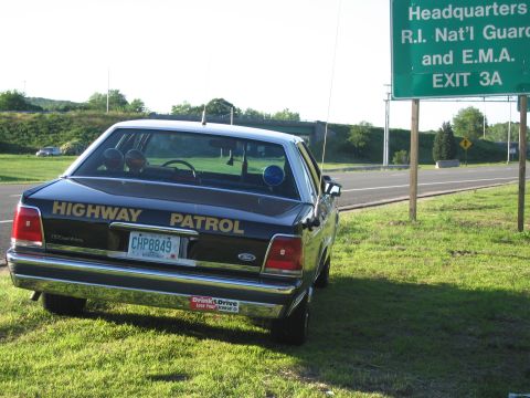 1991 Ford LTD Crown Victoria - rear of a black HIGHWAY PATROL Ford sedan with CHP8849 plate sits on grass next to a green R.I. Nat'l Guard exit sign.