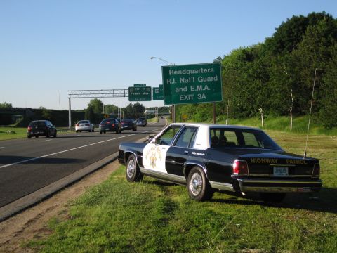 1991 Ford LTD Crown Victoria - black-and-white HIGHWAY PATROL sedan with a star door emblem sits on the grass shoulder as traffic passes on the highway.