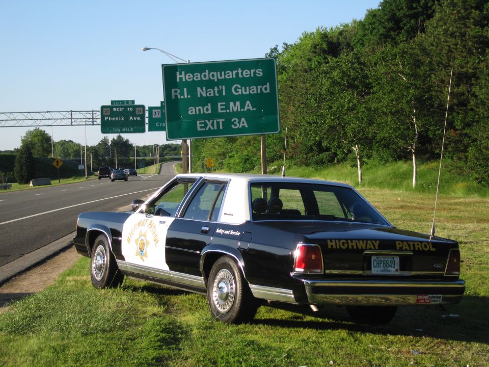 Black-and-white Highway Patrol sedan with star shield parked under a green exit sign