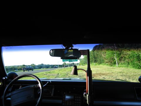 1991 Ford LTD Crown Victoria - Interior view through an older sedan's windshield showing the steering wheel, dash radio, and a highway with green roadside.