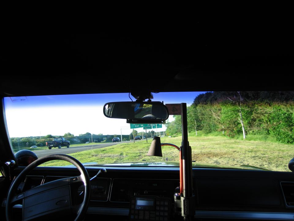 View through windshield of older sedan toward highway and roadside grass