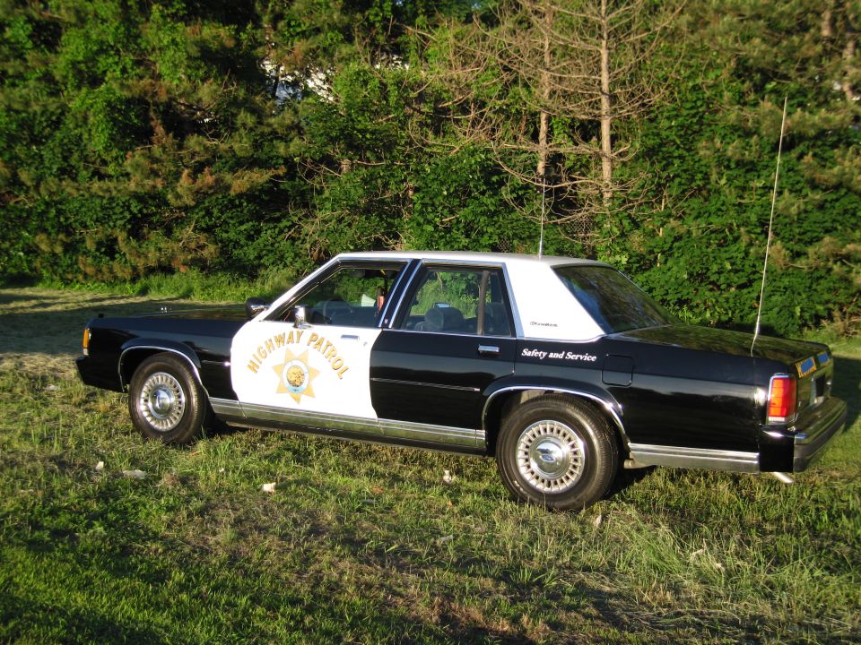 Black and white Highway Patrol sedan parked on grass