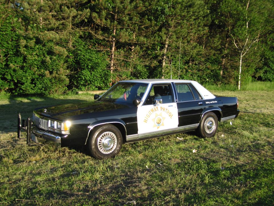 Black and white Highway Patrol sedan with push bar on grass