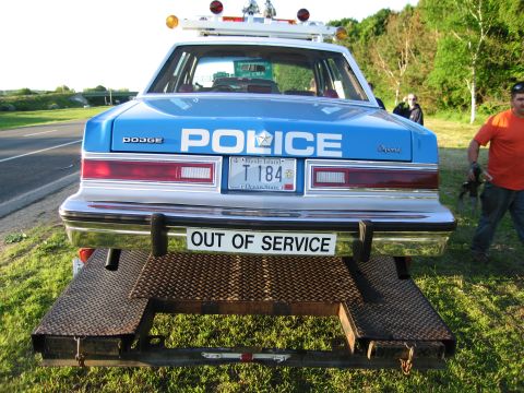 1991 Ford LTD Crown Victoria - Rear view of a blue Dodge Diplomat POLICE car on a trailer with OUT OF SERVICE sign and Rhode Island plate, a man standing nearby.