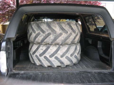 1991 Ford Bronco - Two large, knobby tires are loaded into the back of a vehicle, likely for transport.